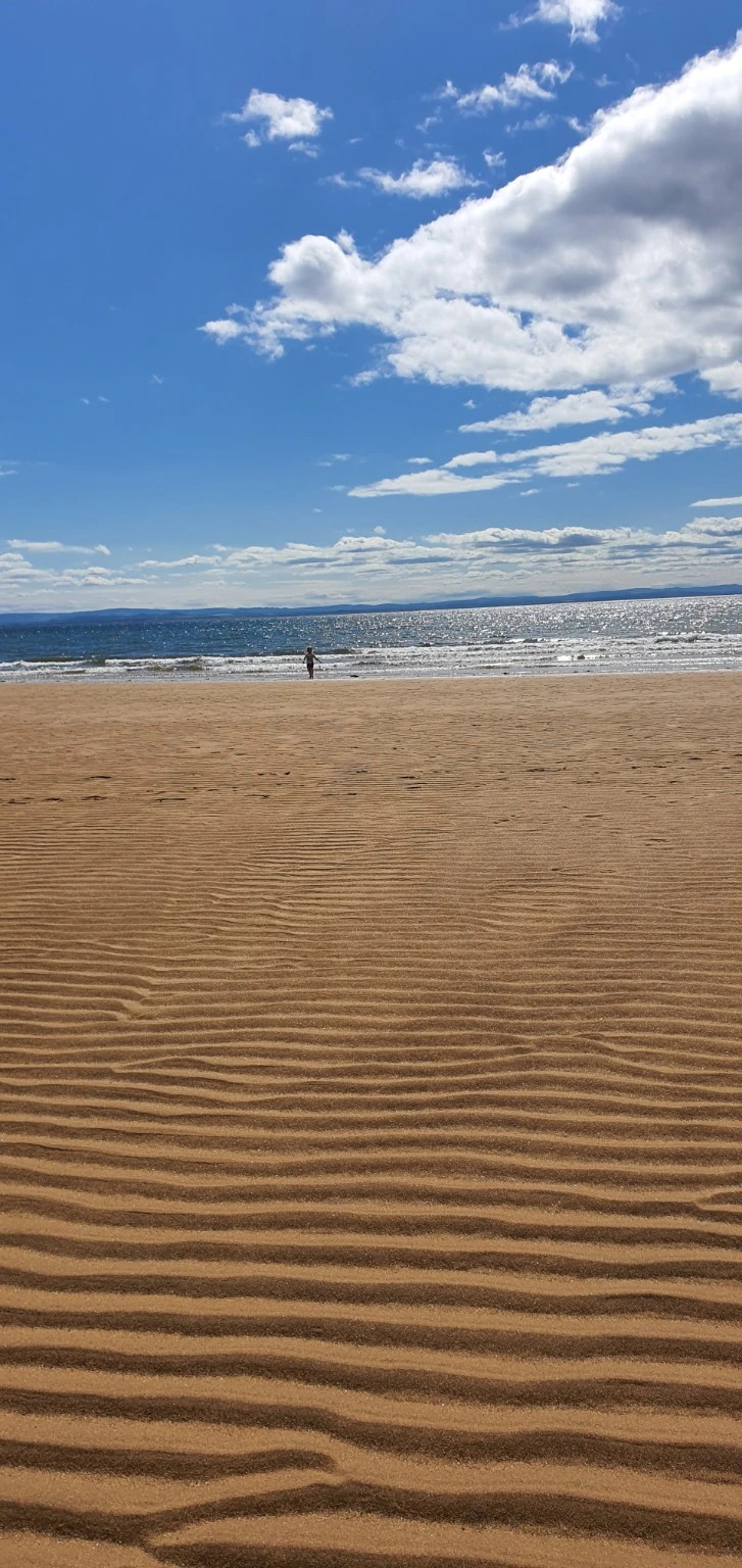 Ripples in the sand, sparkling sea and bright blue sky at the beach